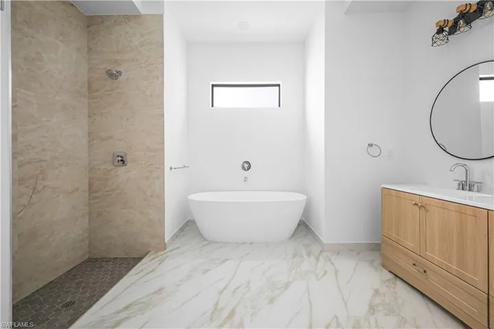 Bathroom featuring a tile shower, a freestanding bath, vanity, and light marble finish floors