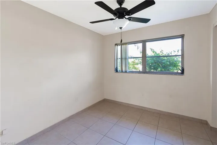 Bedroom featuring light-colored walls, tile flooring, a window providing natural light, and a ceiling fan with integrated lighting