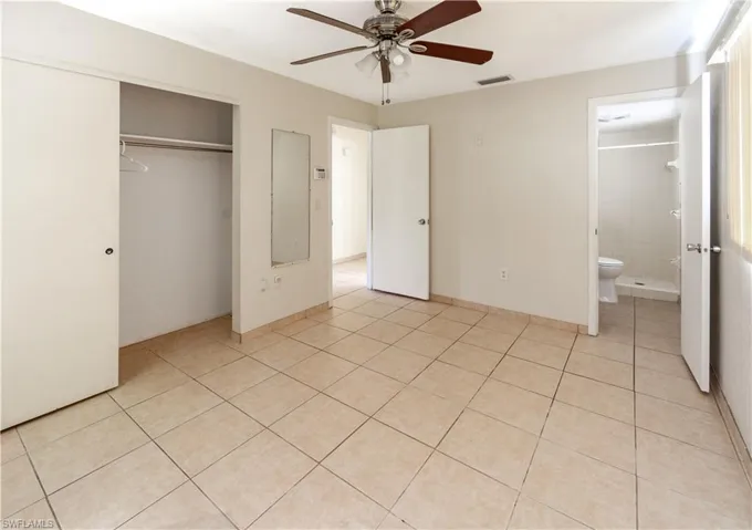 The primary bedroom features light-colored tile flooring, a ceiling fan, and a spacious closet with sliding doors