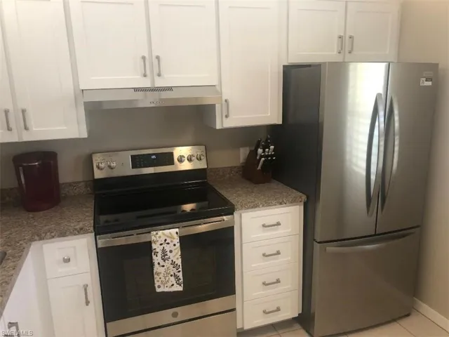 Kitchen with stainless steel appliances, white cabinets, light tile patterned floors, and dark stone countertops