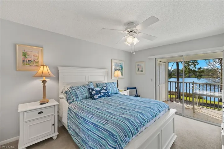 Bedroom with a water view, access to outside, light colored carpet, and a textured ceiling