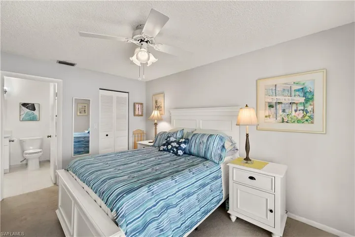 Carpeted bedroom featuring a textured ceiling, connected bathroom, visible vents, a ceiling fan, and a closet