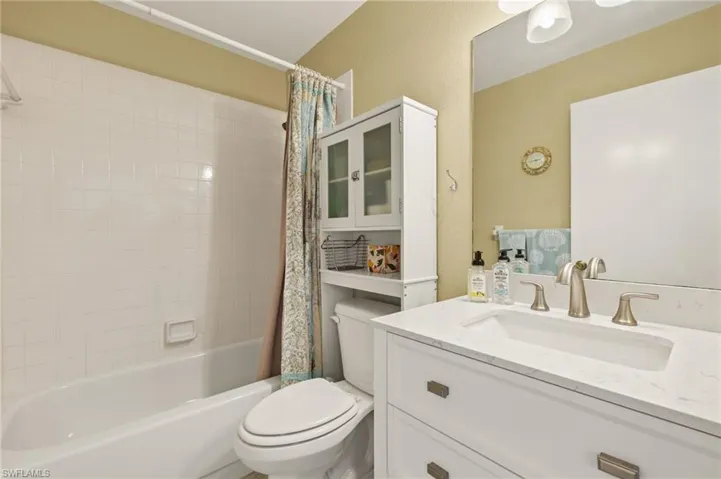 Bathroom featuring a textured wall, shower / tub combo with curtain, toilet, and vanity