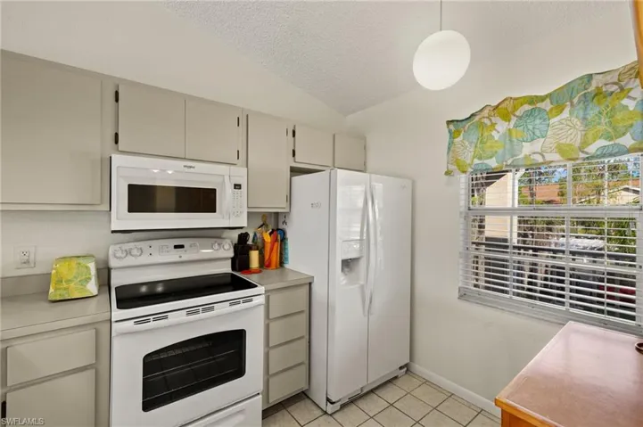 Kitchen with a textured ceiling, light countertops, white appliances, vaulted ceiling, and light tile patterned floors