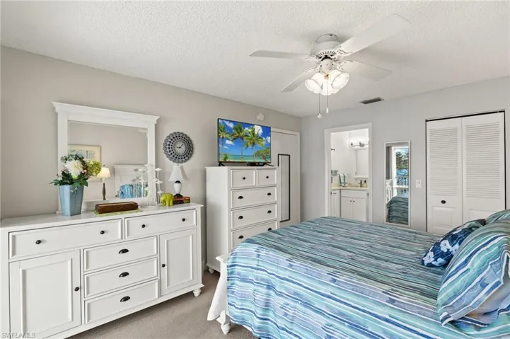 Bedroom with light colored carpet, visible vents, ensuite bath, and a textured ceiling