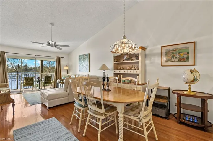 Dining space featuring a textured ceiling, wood finished floors, vaulted ceiling, and ceiling fan with notable chandelier