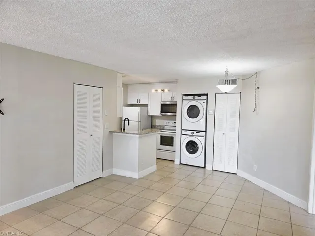 Kitchen with white appliances, white cabinetry, stacked washing machine and dryer, a peninsula, and a textured ceiling