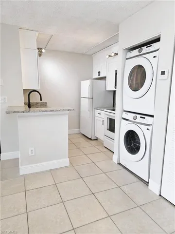 Kitchen with white cabinetry, stacked washer / dryer, a textured ceiling, white electric stove, and light tile patterned flooring