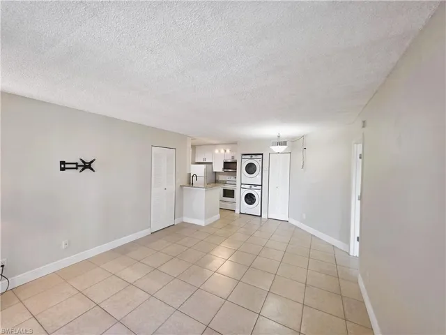Unfurnished living room with stacked washer and clothes dryer, a textured ceiling, and light tile patterned flooring