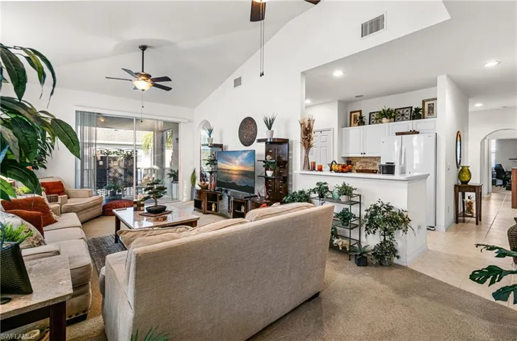 Living room with arched walkways, ceiling fan, light carpet, lofted ceiling, and light tile patterned flooring
