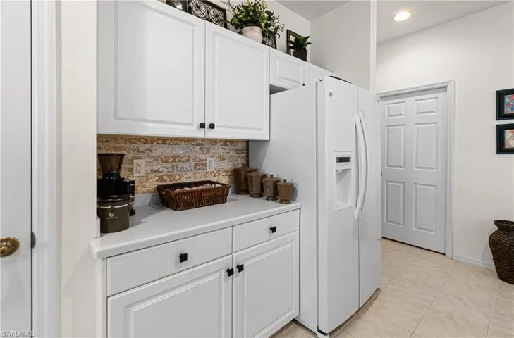 Kitchen with white cabinets, light countertops, decorative backsplash, white refrigerator with ice dispenser, and light tile patterned flooring
