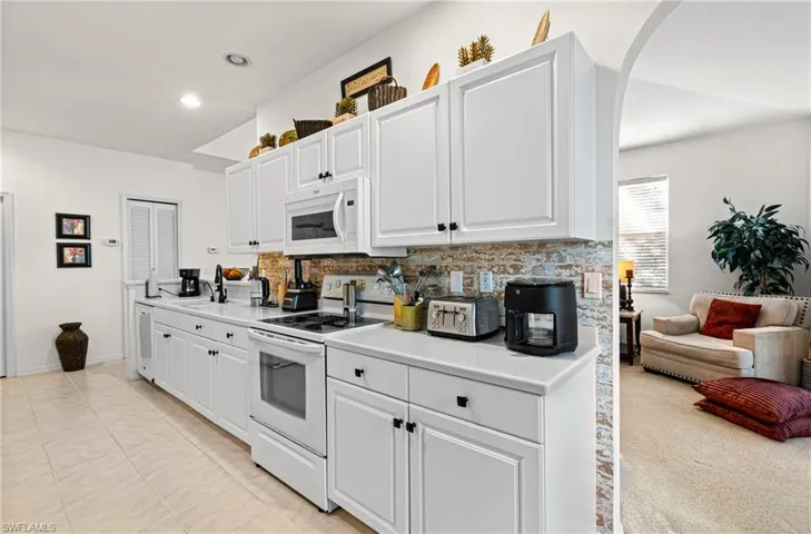 Kitchen featuring white appliances, light countertops, white cabinets, and decorative backsplash
