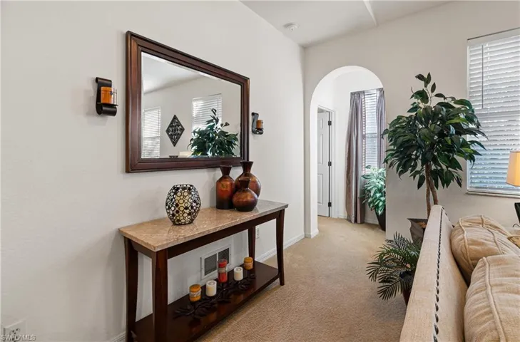 Hall featuring arched walkways, light carpet, and healthy amount of natural light