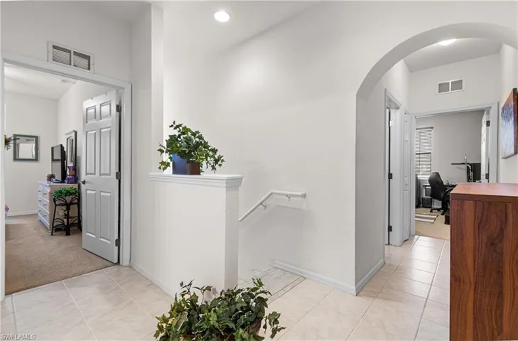 Hall with arched walkways, light tile patterned flooring, and an upstairs landing