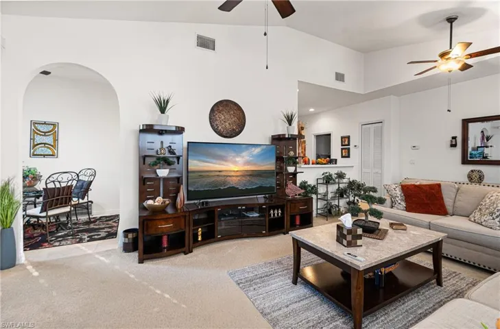Living area featuring arched walkways, vaulted ceiling, a ceiling fan, and carpet flooring