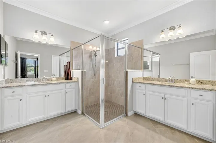 Full bath with crown molding, a shower stall, two vanities, and tile patterned flooring