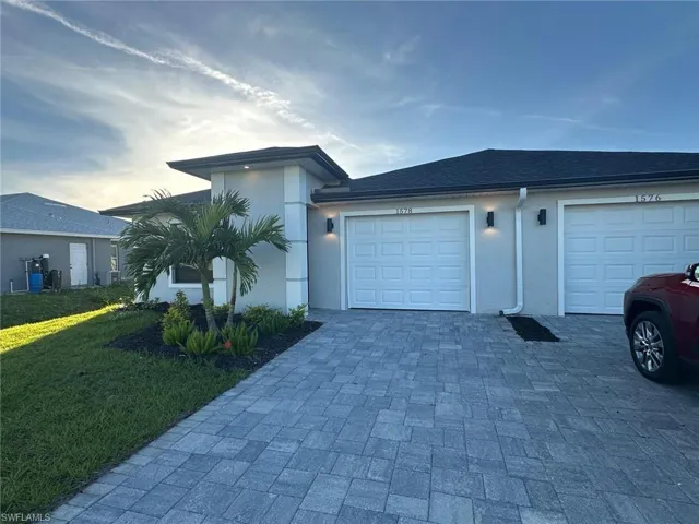 View of front of house with decorative driveway, stucco siding, a front lawn, and a garage