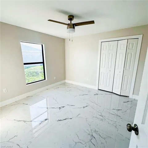 Unfurnished bedroom featuring light marble finish floors, ceiling fan, and a closet