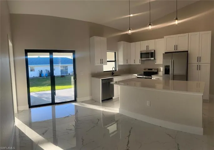 Kitchen with light marble finish floors, stainless steel appliances, white cabinets, pendant lighting, and a kitchen island