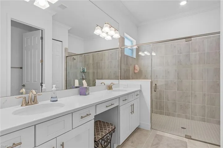 Bathroom featuring ornamental molding, dual vanity, and an enclosed shower