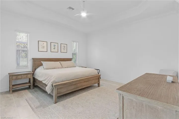 Tiled bedroom with a raised ceiling, multiple windows, and ornamental molding
