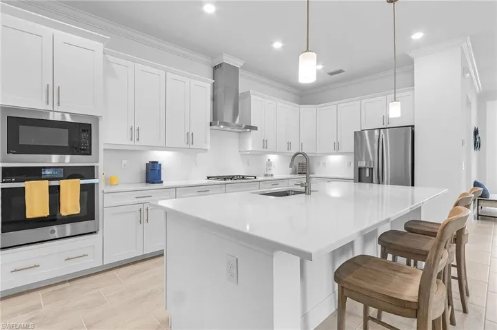 Kitchen with appliances with stainless steel finishes, white cabinets, wall chimney range hood, and a center island with sink