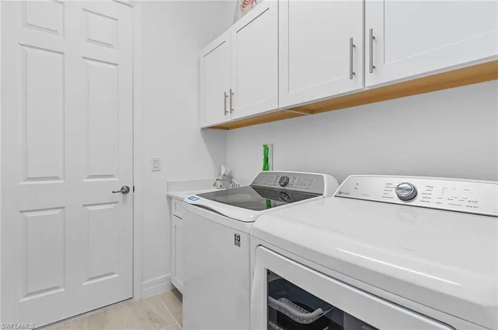 Clothes washing area with cabinets, sink, light tile patterned floors, and independent washer and dryer
