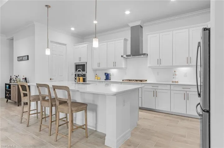 Kitchen featuring crown molding, stainless steel appliances, white cabinets, decorative light fixtures, and wall chimney exhaust hood