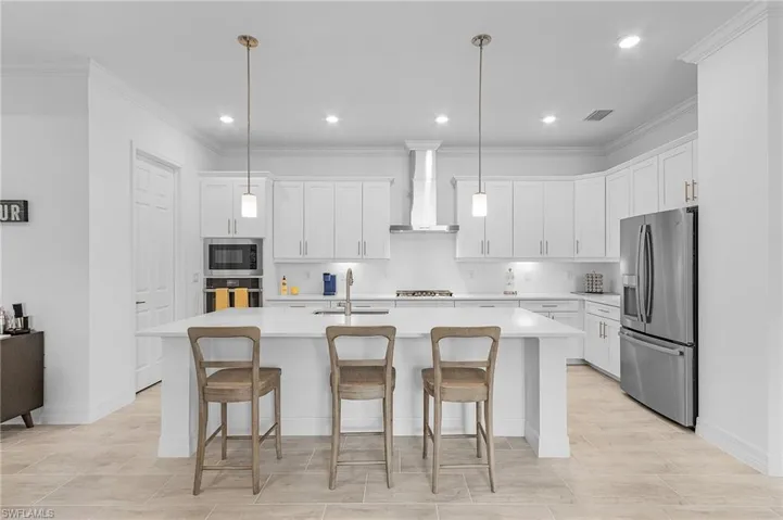 Kitchen with appliances with stainless steel finishes, wall chimney range hood, hanging light fixtures, a center island with sink, and sink