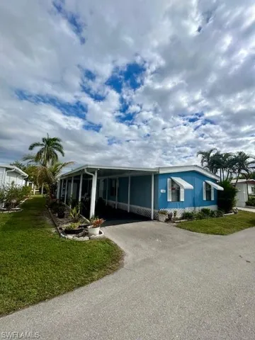 Manufactured / mobile home with a front lawn, asphalt driveway, a carport, and a sunroom