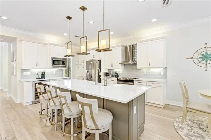 Kitchen with backsplash, appliances with stainless steel finishes, a kitchen island with sink, wall chimney range hood, and beverage cooler