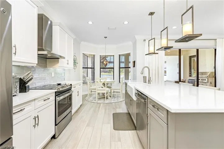 Kitchen with appliances with stainless steel finishes, pendant lighting, wall chimney exhaust hood, and light wood-type flooring