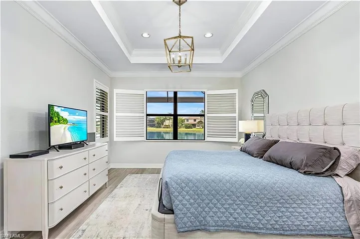 Bedroom with crown molding, light hardwood / wood-style flooring, a raised ceiling, and a chandelier