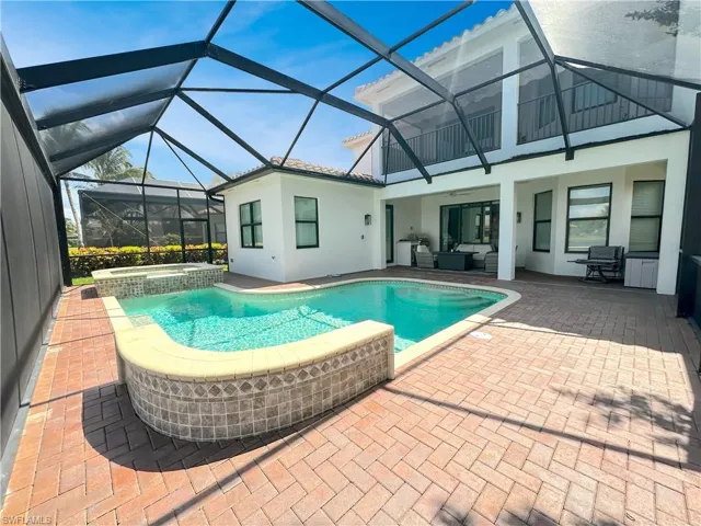 View of pool with glass enclosure, a patio area, and an in ground hot tub