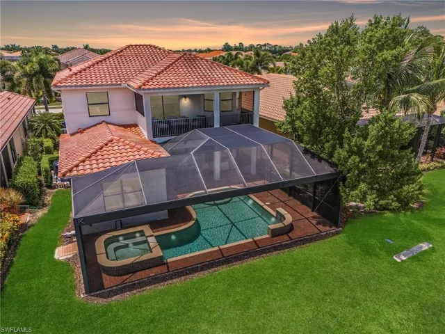 Back house at dusk with a swimming pool with hot tub, a lanai, a yard, and a patio