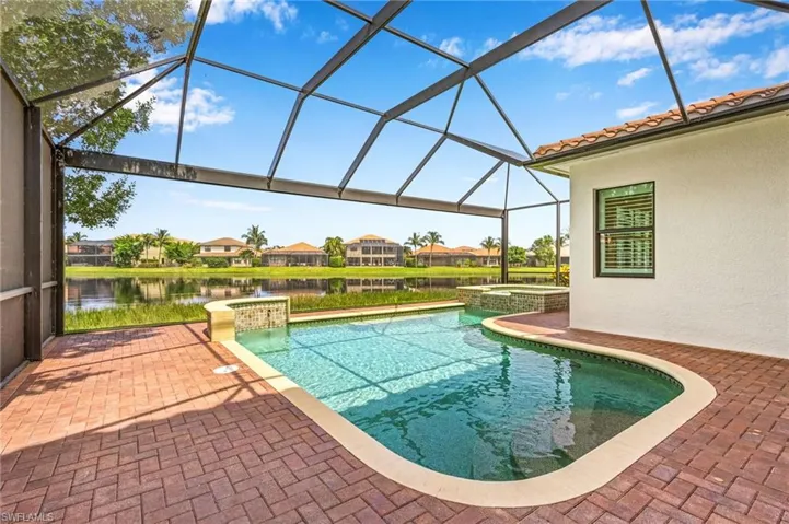 View of pool featuring a water view, a patio area, glass enclosure, and an in ground hot tub