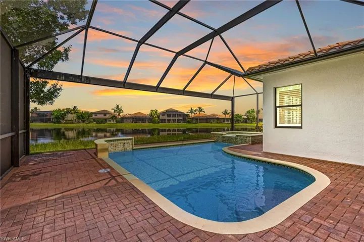 Pool at dusk with a patio area, an in ground hot tub, a water view, and glass enclosure