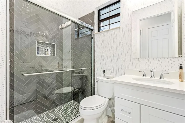 Bathroom with a shower with shower door, vanity, and toilet
