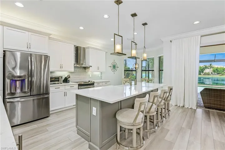 Kitchen featuring appliances with stainless steel finishes, a wealth of natural light, an island with sink, and wall chimney range hood