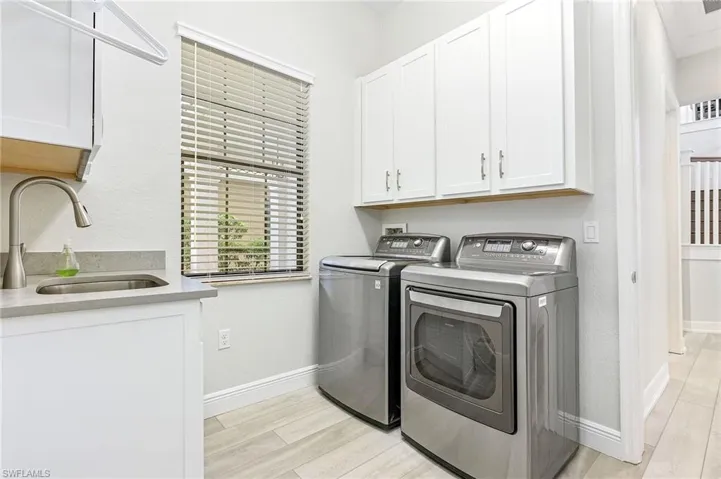 Clothes washing area featuring sink, light hardwood / wood-style floors, separate washer and dryer, and cabinets