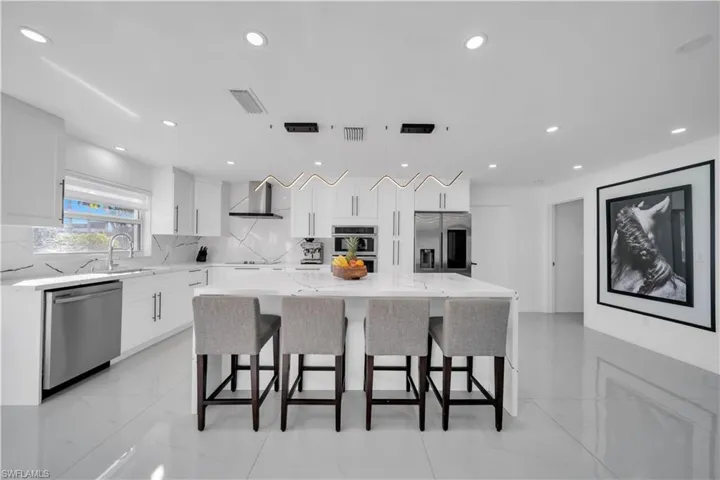 Kitchen with stainless steel appliances, a kitchen island, light stone countertops, pendant lighting, and white cabinets