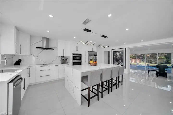 Kitchen featuring light stone countertops, a kitchen island, white cabinets, stainless steel appliances, and a kitchen bar