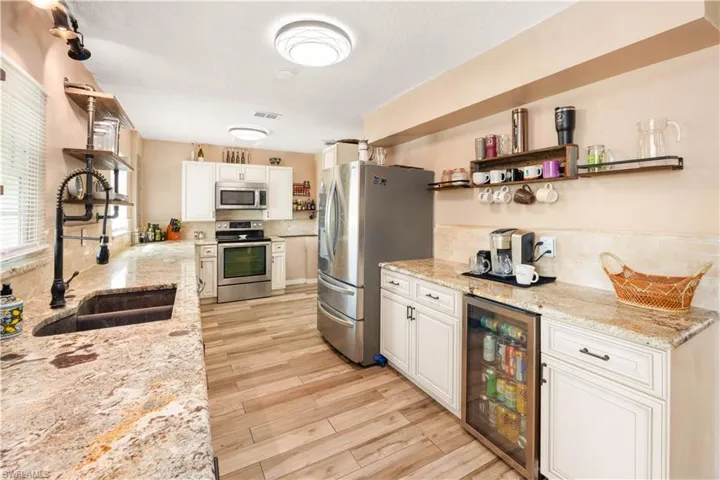 Kitchen featuring beverage cooler, granite counters, appliances with stainless steel finishes, custom cabinetry