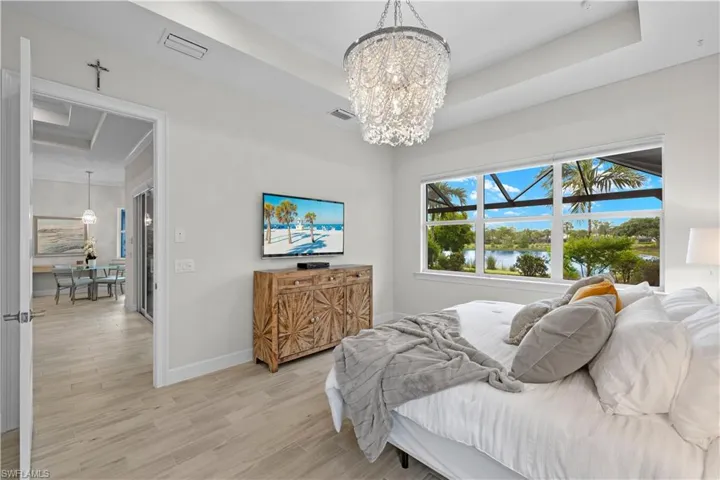 Owners Suite Bedroom featuring an inviting chandelier, multiple windows with motorized shades, and a tray ceiling