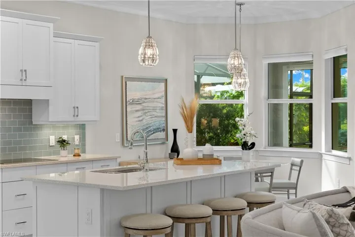 Open kitchen featuring a breakfast nook, pendant lighting, white cabinets, sink, backsplash, and a kitchen island with sink and breakfast bar