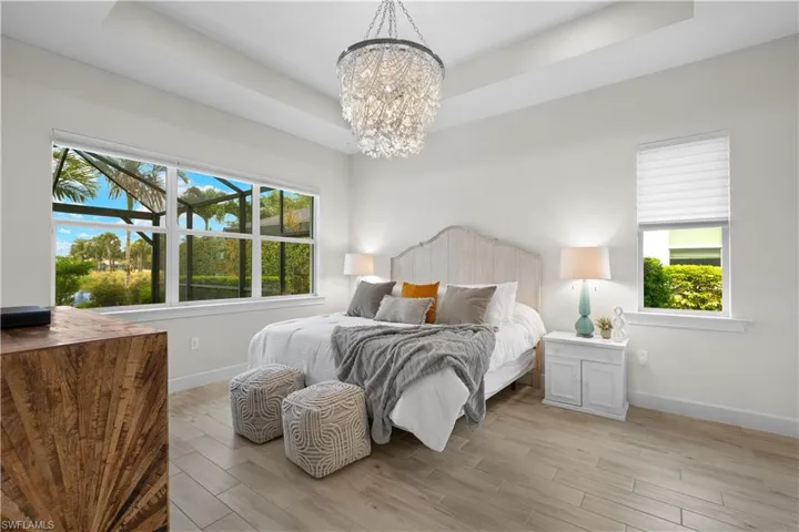 Owners Suite Bedroom featuring an inviting chandelier, multiple windows with motorized shades, and a tray ceiling