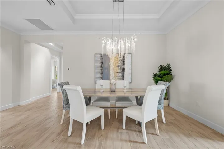 Dining room featuring light wood-style tile floors, crown molding, Swarovski chandelier, and a tray ceiling