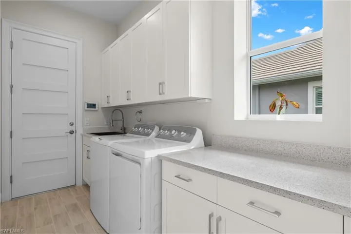 Bright laundry room with extra upper cabinet storage, stainless steel sink, washing machine and dryer