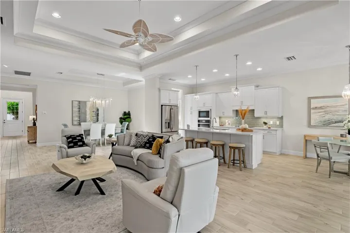 Living room featuring double tray ceilings with crown molding, wood-style tile flooring, and ceiling fan