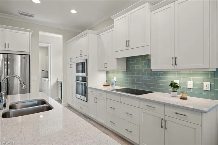 Kitchen featuring white cabinetry, tasteful backsplash, crown molding, sink, and appliances with stainless steel finishes